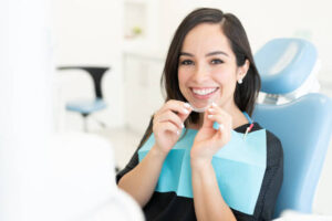 Woman holding a clear aligner while sitting in dentist’s chair